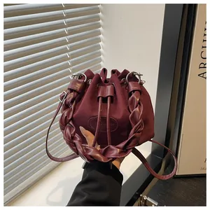 Close-up of burgundy suede bucket bag featuring drawstring closure and woven handle detail