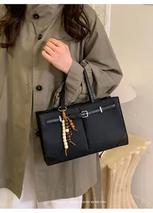 Detail of a black textured tote bag with leather buckle and colorful wooden bead tassel