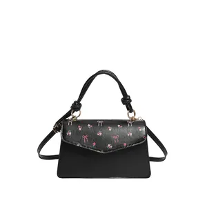Chic black crossbody bag featuring pink floral bow pattern and gold-tone hardware detail
