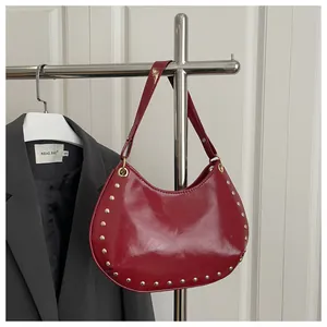 Detail view of red semi-circle underarm bag featuring glossy leather and gold rivets