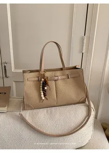 Detail of a beige woven tote bag with bead tassel charm and adjustable strap on a white sofa
