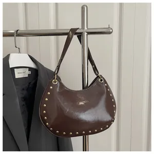 Detail of brown patent leather hobo bag with gold rivet studs and metallic ring strap