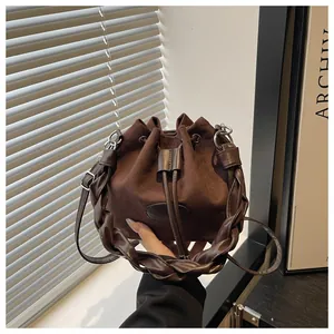 Detail of dark brown suede bucket bag featuring woven leather handle and fashion label