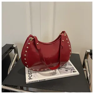 Detailed macro of a red patent leather half moon bag featuring gold stud ornaments