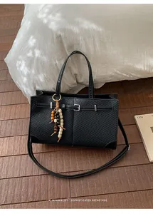 Close-up of black textured tote bag with wood bead tassel on a wooden floor