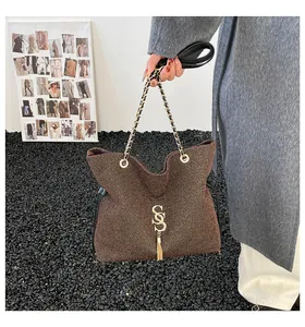Detalle de bolso tote marrón texturizado con logo SSS dorado, flecos y cadena
