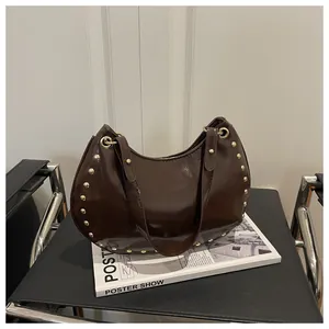 Detail of dark brown glossy shoulder bag with golden rivets on a minimalist setup