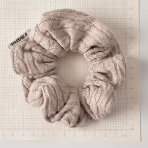 Détail du chouchou en tricot kaki avec texture torsadée et étiquette sur fond quadrillé