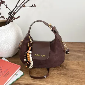 Sac hobo en daim marron café avec bordure en cuir et perles déco sur table en bois