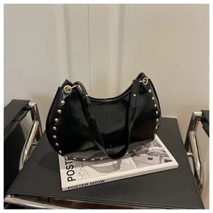 Detail of black patent leather crescent bag with golden studs on a black chair