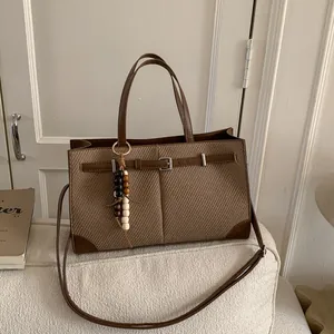 Brown woven tote bag with leather trim and beaded charm on a minimalist sofa
