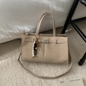 Beige woven tote bag with leather trim and beaded pendant in a cozy home setting