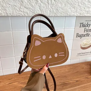 Cute brown cat-shaped crossbody bag with pink embroidery and top handle on wood table