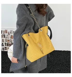 Detalle de bolso tote amarillo con logo SS dorado, borla y correa de cadena en modelo