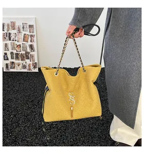 Detalle de bolso amarillo texturizado con logo SS, cadena dorada y borla elegante