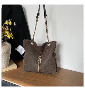 Detalle de bolso glitter marrón con borla dorada y logo de metal en mesa de madera