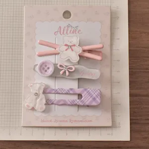 Detailliertes Set aus 3 Pastell-Haarspangen mit Bär, Schleife und Karomuster auf Karte