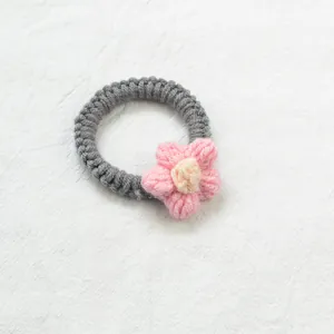 Détail d'un chouchou en tricot gris avec fleur au crochet rose sur fond de tissu blanc