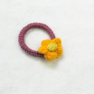Détail d'un élastique à cheveux tricoté main avec ruban violet et fleur orange vive