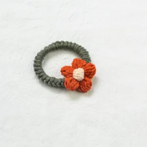 Gros plan sur un chouchou au crochet fait main en laine vert foncé avec fleur orange