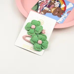 Détail de deux barrettes fleurs en tissu vert fait main sur une carte de présentation