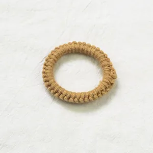 Détail d'un chouchou en tricot camel tissé main avec texture sur fond en lin blanc