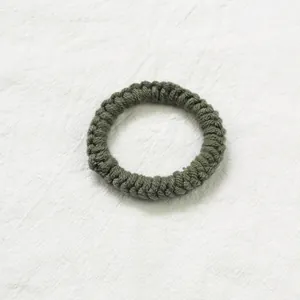 Texture détaillée d'un chouchou spirale tricoté main vert foncé sur tissu blanc