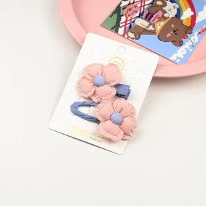 Détail de pinces à cheveux fleurs en tissu rose avec broderie sur une carte de vente