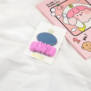 Detail of blue denim and pink pleated hair clips set on a white display card