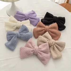 Flat lay of seven knit mohair bow hair clips in assorted soft pastel colors on white fabric