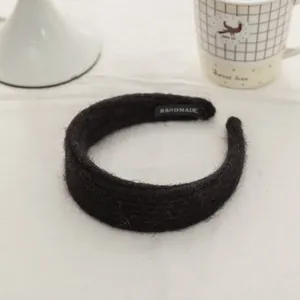Detail of a thick black mohair knit headband with a handmade label on a white table