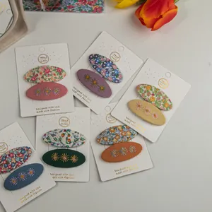 Détail de barrettes en tissu brodé de fleurs présentées sur une carte artisanale