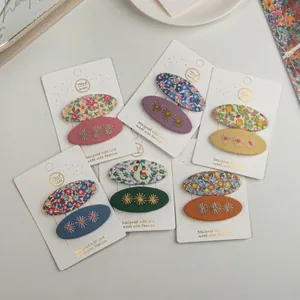 Vue à plat de lots de 2 barrettes en tissu brodé de fleurs aux couleurs pastel variées