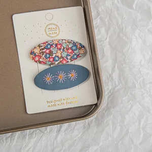 Détail de deux barrettes en tissu à broderie florale sur une carte blanche dans un plateau
