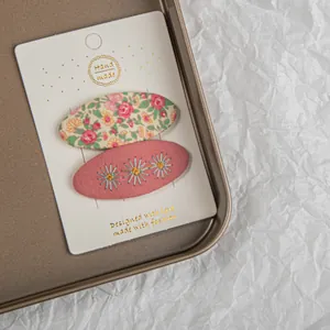 Détails de deux barrettes en tissu à broderie florale sur carte blanche