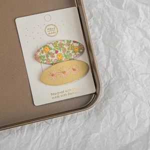 Détail de pinces à cheveux en tissu imprimé et broderie florale sur carte blanche