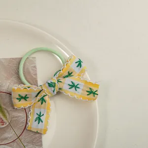 Détail d'un chouchou vert avec nœud à carreaux jaunes et broderie florale douce