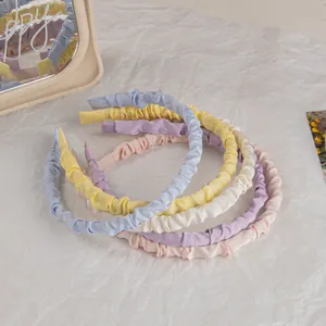 Pleated satin headbands in pastel colors displayed on a white textured background