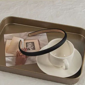 Detail view of a thick black satin headband resting on a coffee cup and vintage postcard