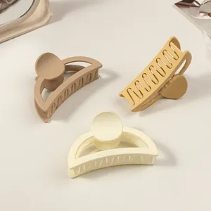 Macro detail of three matte cream-colored hair claw clips for long hair on white backdrop