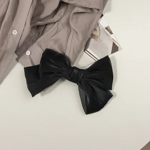 Détail d'une barrette à cheveux nœud noir en satin sur une chemise et un magazine
