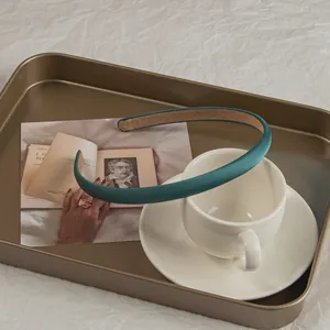 Detail of peacock green satin headband showing non-slip lining on a gold tray