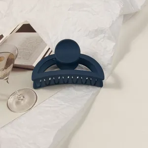 Detailed close-up of matte dark blue shark clip hair claw on aesthetic paper and glass