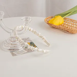 Detailed close-up of cream-colored pleated satin headband with a soft ruffled texture