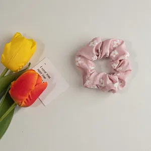 Detail eines rosa Haar-Scrunchie mit weißen Blumenmustern und weicher Stofftextur