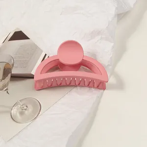 Detail of a large matte pink hair claw clip on a white background with lifestyle props