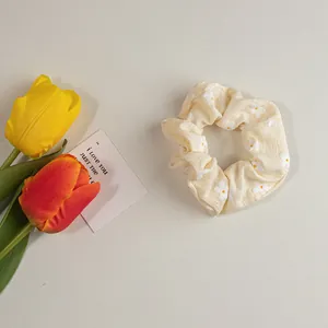 Detail eines hellgelben Blumen-Haargummis mit weißem Gänseblümchenmuster aus weichem Stoff