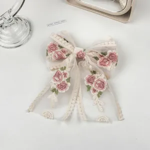 Detail view of mesh bow hair clip featuring delicate pink flower embroidery on beige fabric