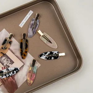 Set of six colorful acetate hair clips with marble patterns on a vintage metal tray