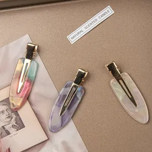 Macro detail of tortoiseshell acetate duckbill hair clips with marbled texture and gold metal